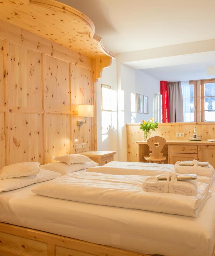 Wood-panelled Romantic Suite with a double bed, towels laid out on the bed, a seating area and a window with views of the Dolomites.