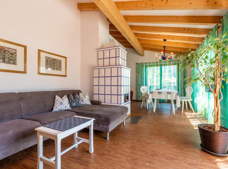 Soggiorno della Suite Panorama con divano grigio, tavolino bianco, soffitto con travi in legno e piante rampicanti davanti alla zona pranzo vicino alla finestra.