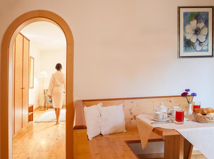 Family Suite con angolo soggiorno in legno chiaro, tavolo apparecchiato per la colazione e passaggio ad arco.