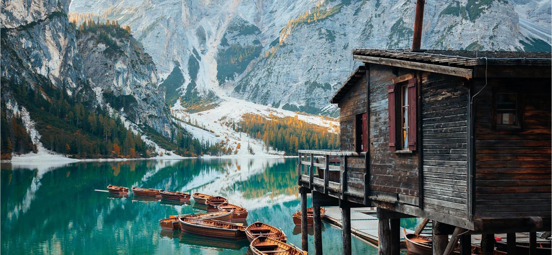Pragser Wildsee mit Bootshaus und Booten im Vordergrund und markanten Bergen im Hintergrund.